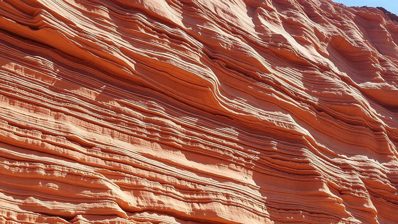 Layered sedimentary rock strata exposed in a bright sunlit cliff face